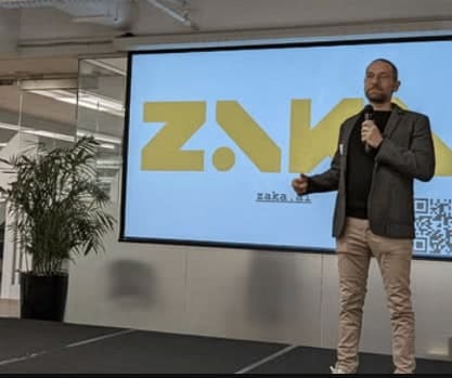 A ZAKA consultant presenting on stage in front of the ZAKA logo